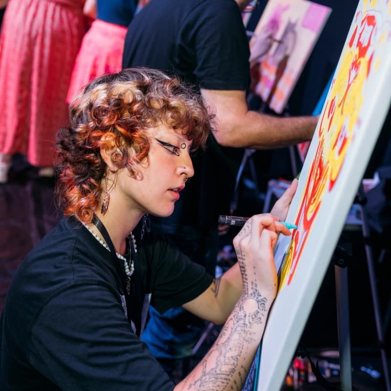 An artist with curly hair painting on a canvas at an easel during Art Battle Bournemouth