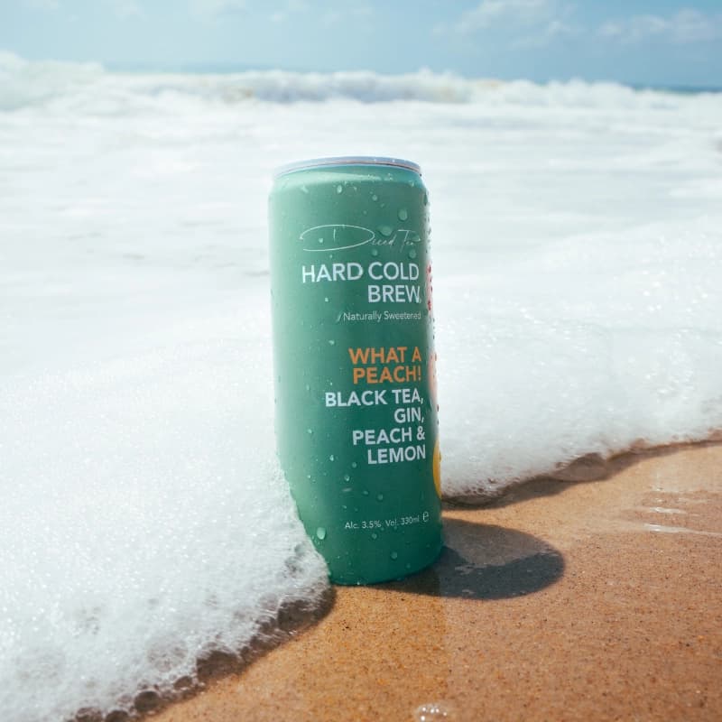 A can of Diced Tea hard cold brew standing in the surf on a sunny beach